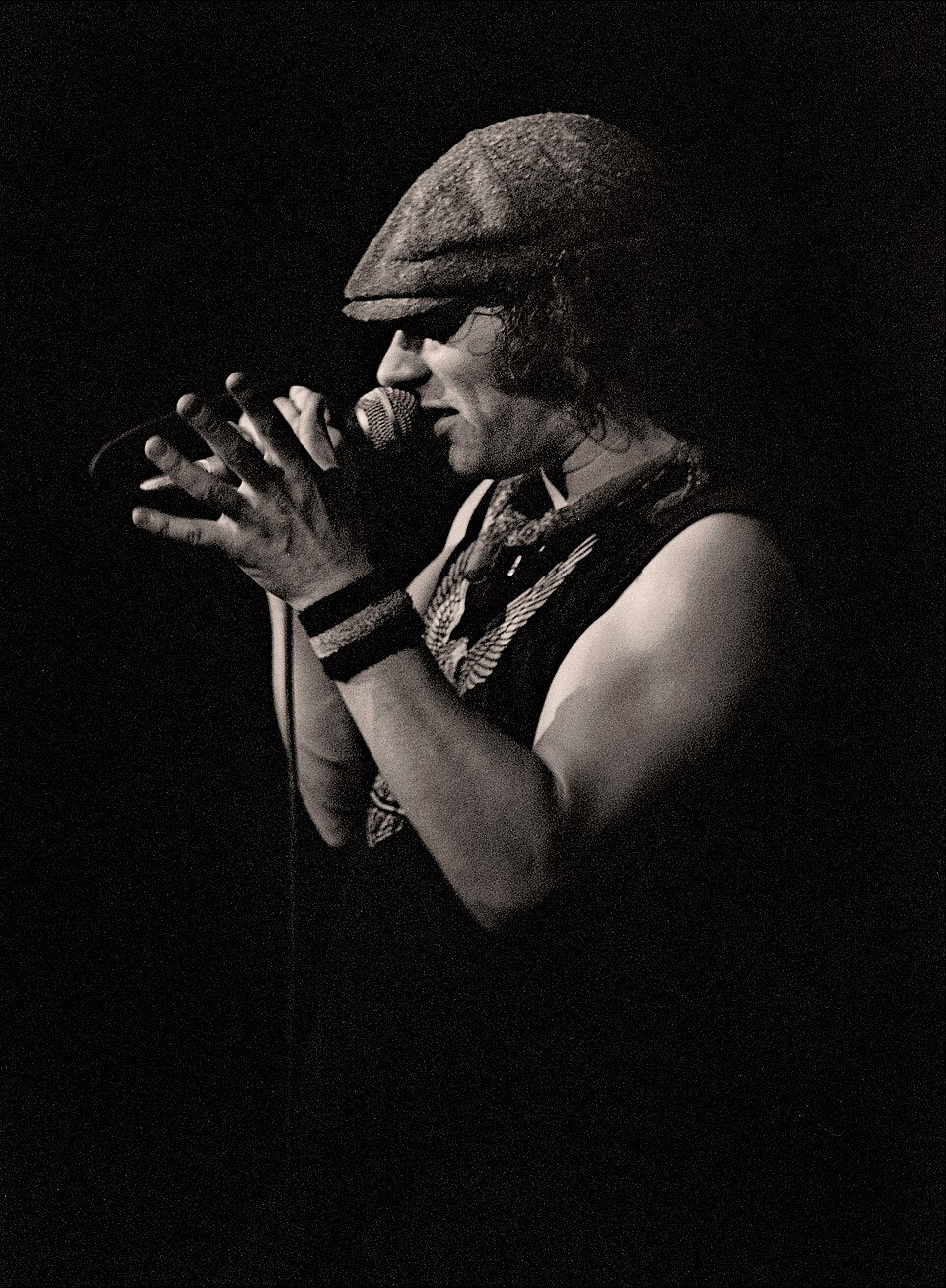 Zwart-witfoto van Brian Johnson die met zijn kenmerkende pet een handmicrofoon vasthoudt.