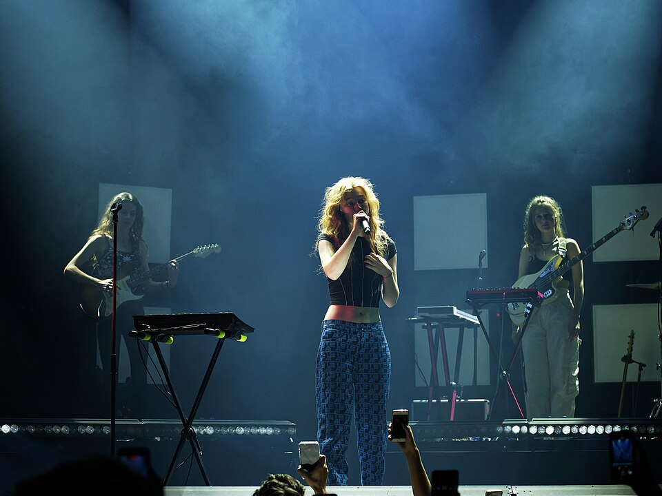 Froukje zingt met haar band op een blauw verlicht podium, met een microfoon in haar hand.