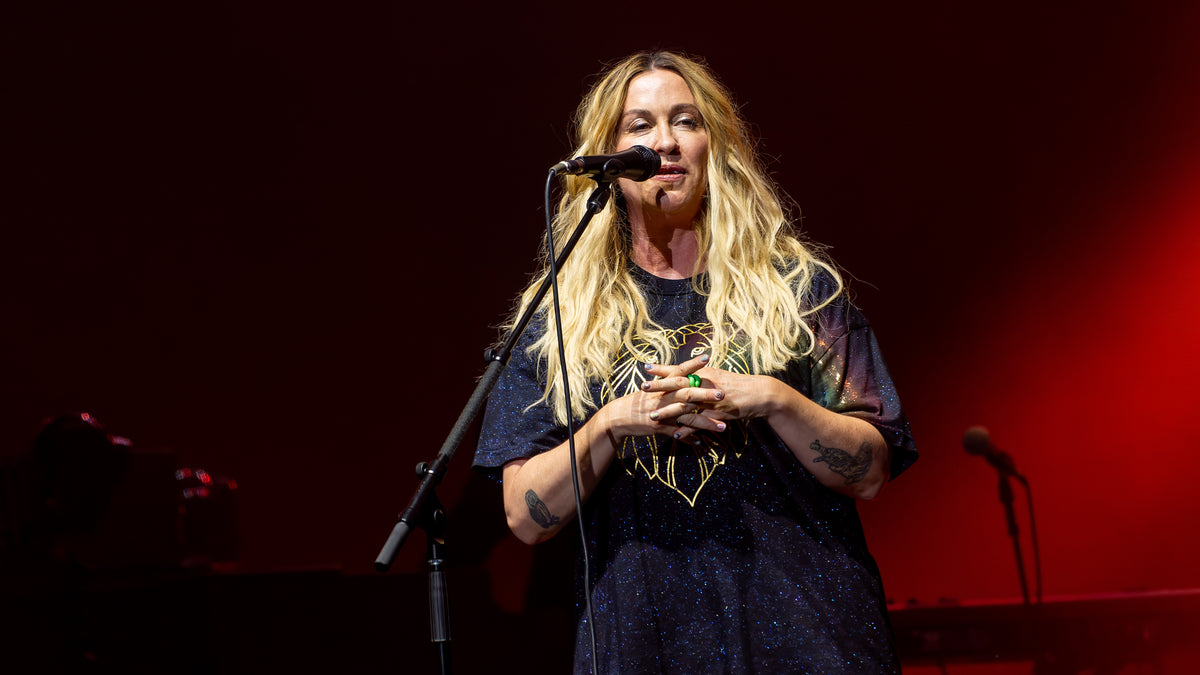 Alanis Morissette staat achter een microfoon op een rood verlicht podium.