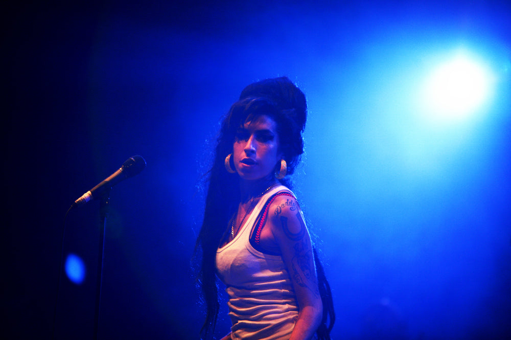 Amy Winehouse naast een microfoon op een podium in blauw licht.