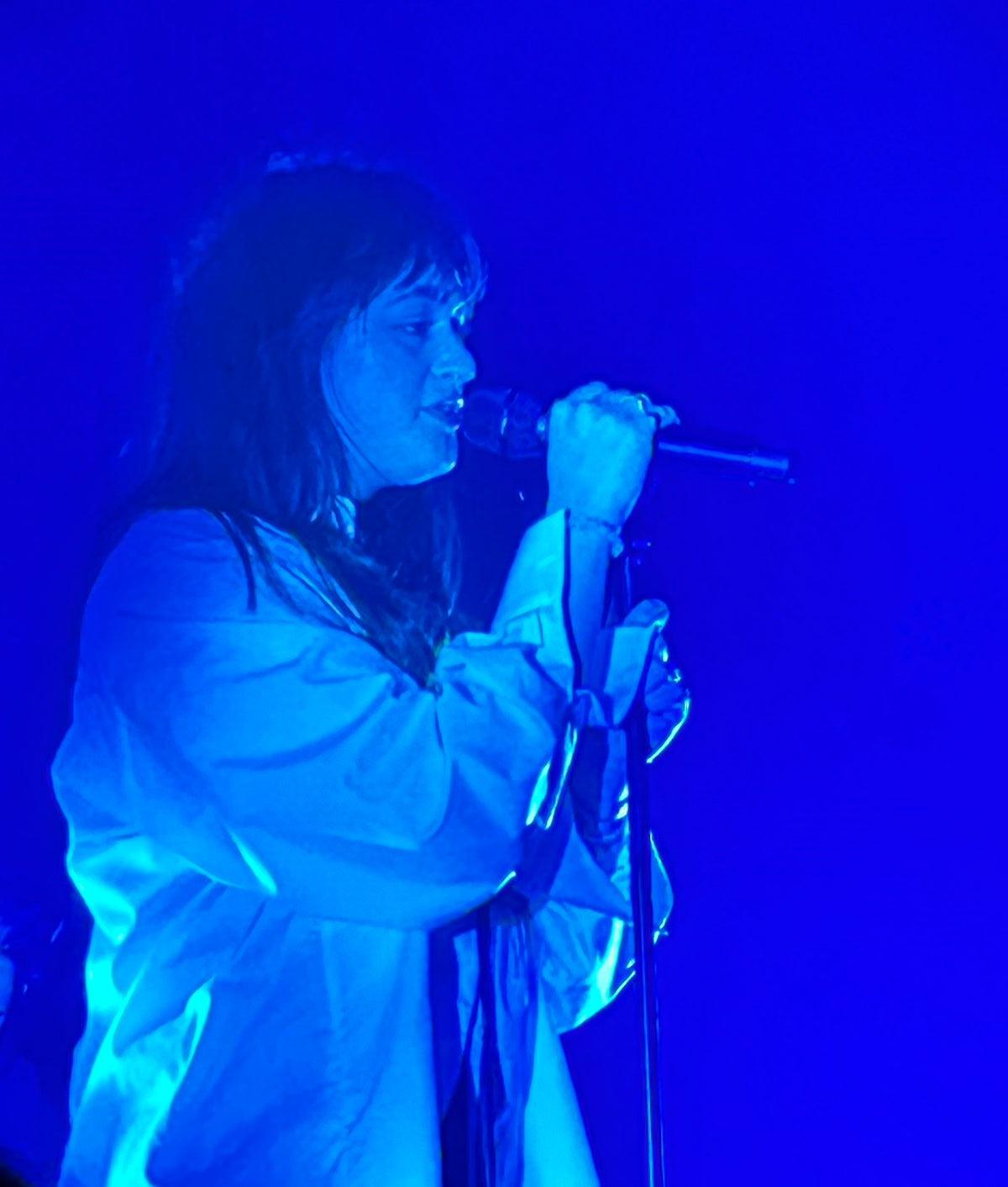 Bente zingt in een microfoon, verlicht door blauw podiumlicht.