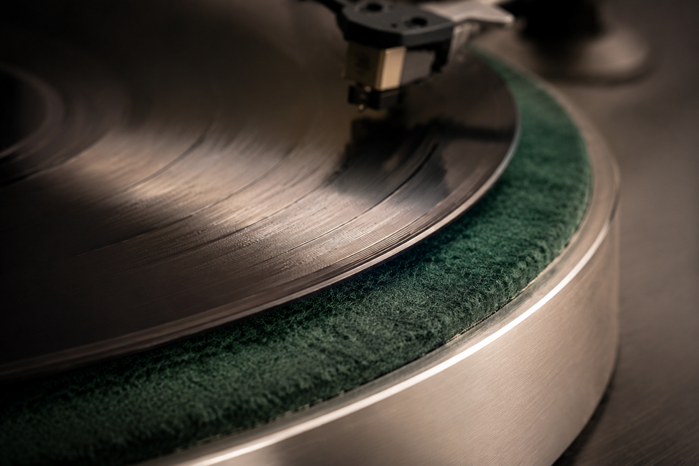 Detailopname van een zwarte vinylplaat op een groene vilten slipmat en aluminium draaiplateau.