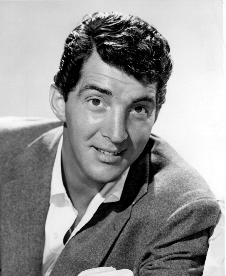 Dean Martin kijkt glimlachend naar de camera in een jasje met open kraag