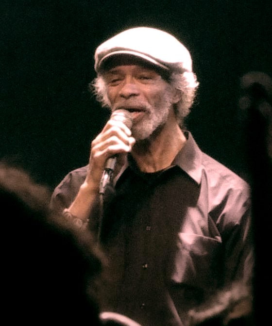 Gil Scott-Heron zingt met een microfoon in zijn hand.