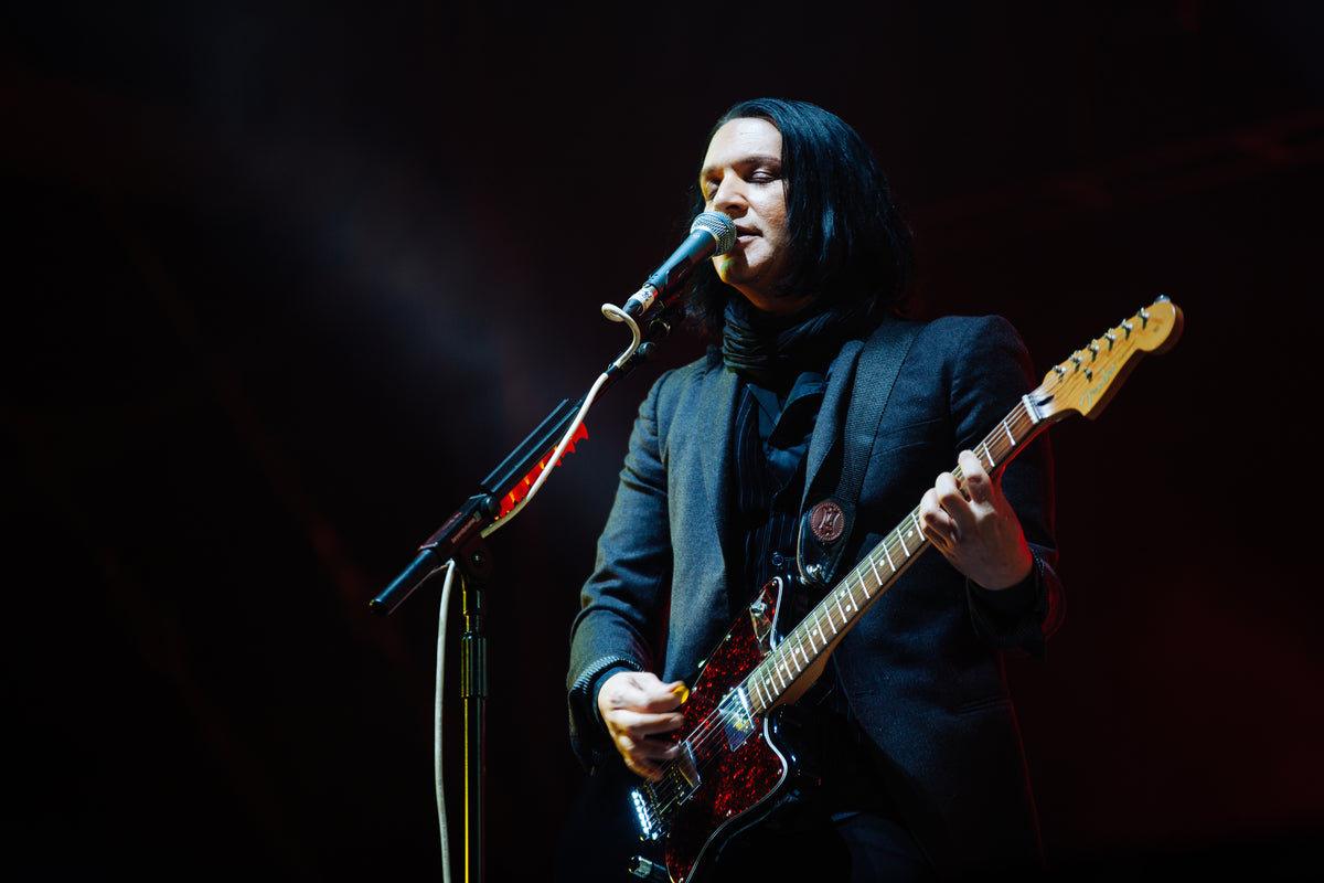 Brian Molko zingt en speelt gitaar tijdens een optreden van Placebo in 2014