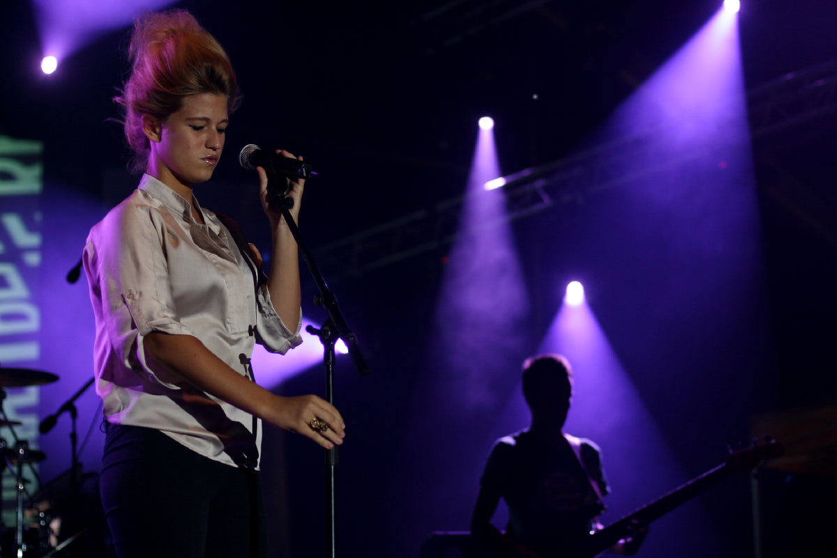 Selah Sue zingt in een witte blouse bij een microfoon op Sziget in 2011, met paarse podiumlichten en een muzikant achter haar.