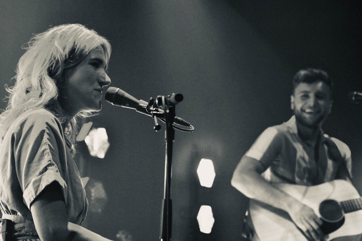 Suzan zingt bij een microfoon terwijl Freek rechts gitaar speelt