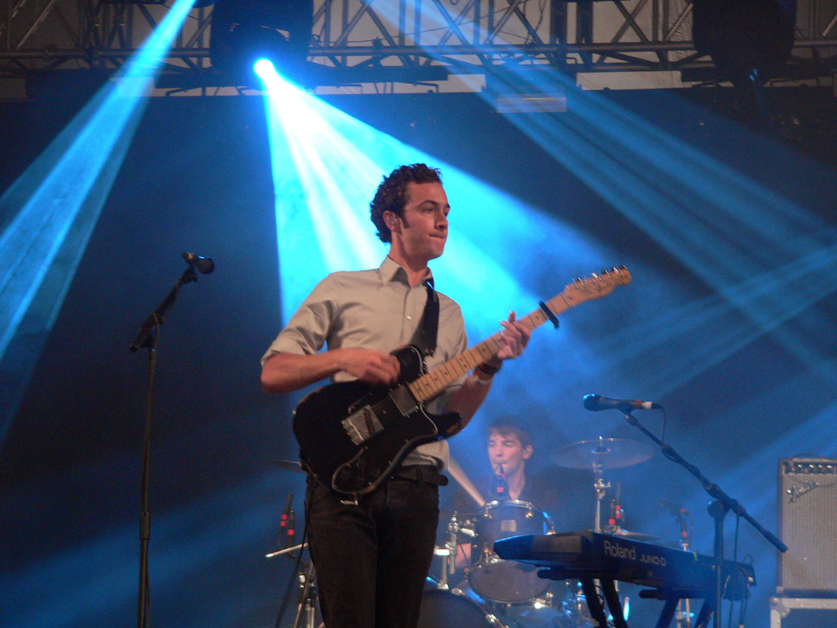 Tom Smith speelt gitaar met Editors onder blauw podiumlicht op Roskilde Festival