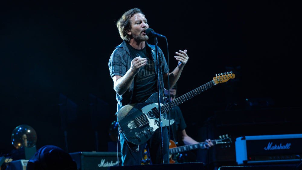 Eddie Vedder zingt met een gitaar om zijn schouder op een blauw verlicht podium.