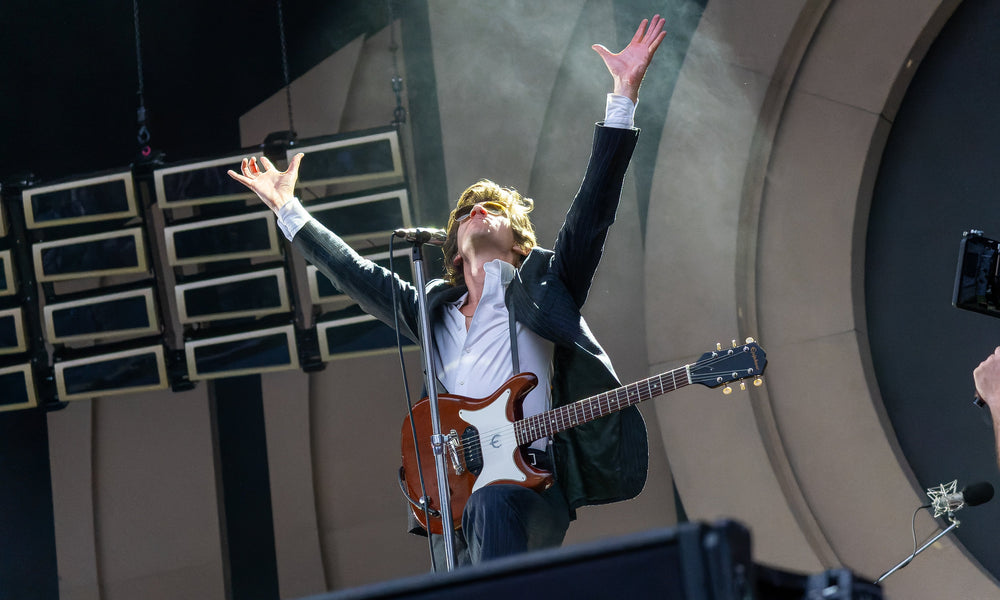 Alex Turner met gitaar en opgeheven armen tijdens een optreden van Arctic Monkeys in Londen.