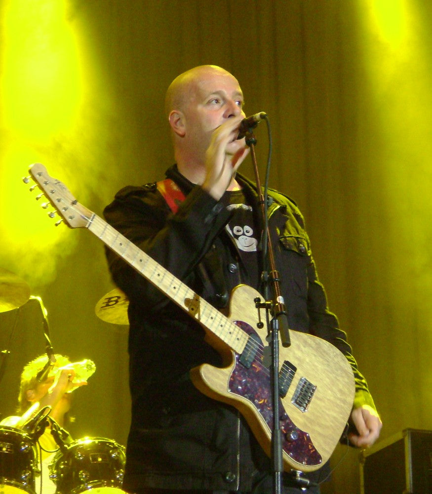 Paskal Jakobsen met gitaar en microfoon in geel podiumlicht.