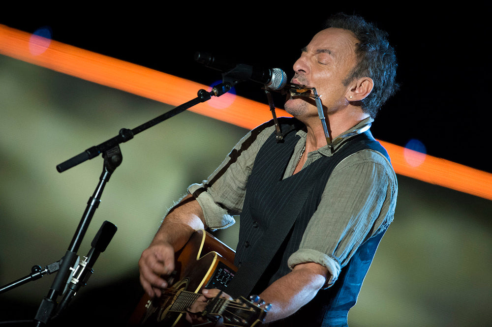 Bruce Springsteen met akoestische gitaar en mondharmonica op het podium
