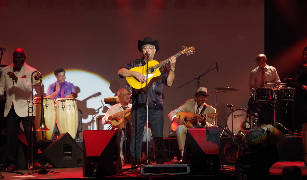 Eliades Ochoa zingt en speelt gitaar met de Orquesta Buena Vista Social Club op een podium.