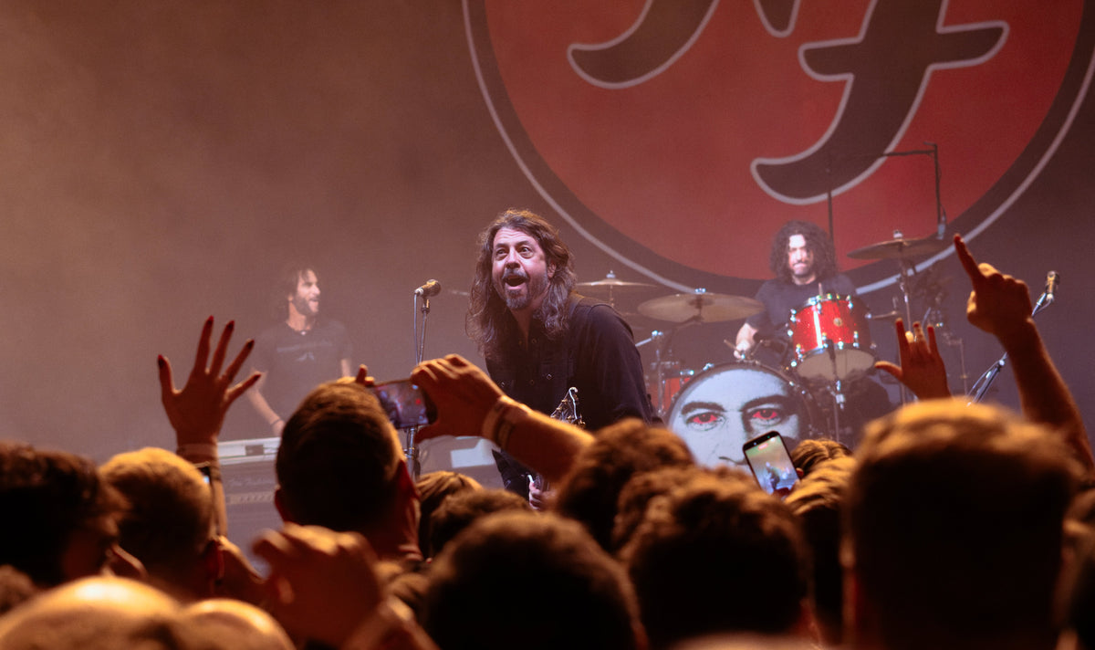 Dave Grohl bij de microfoon, met Foo Fighters achter hem en opgestoken handen uit het publiek op de voorgrond.