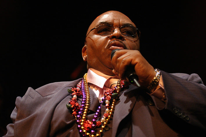 Solomon Burke zingt met een handmicrofoon tegen een donkere podiumachtergrond.