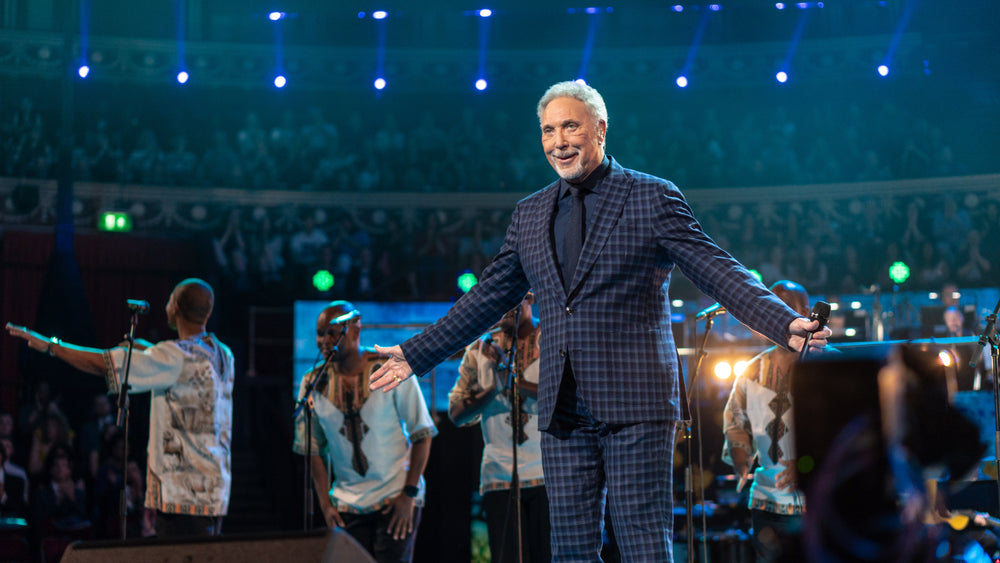 Tom Jones staat met gespreide armen en een microfoon op het blauw verlichte podium van de Royal Albert Hall.