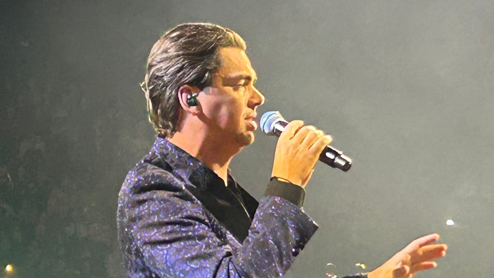 Yves Berendse zingt met een microfoon in een glanzend blauw jasje tijdens het Muziekfeest van het Jaar. Foto: Martijn van den Baar, CC BY-SA 4.0; uitsnede.