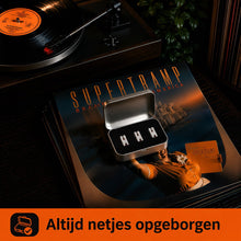 Opbergdoosje met drie witte naalden naast vinylplaten. Platenspeler naald in gebruik.