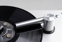 Close-up van een zilveren reinigingsarm op een draaiende vinylplaat.