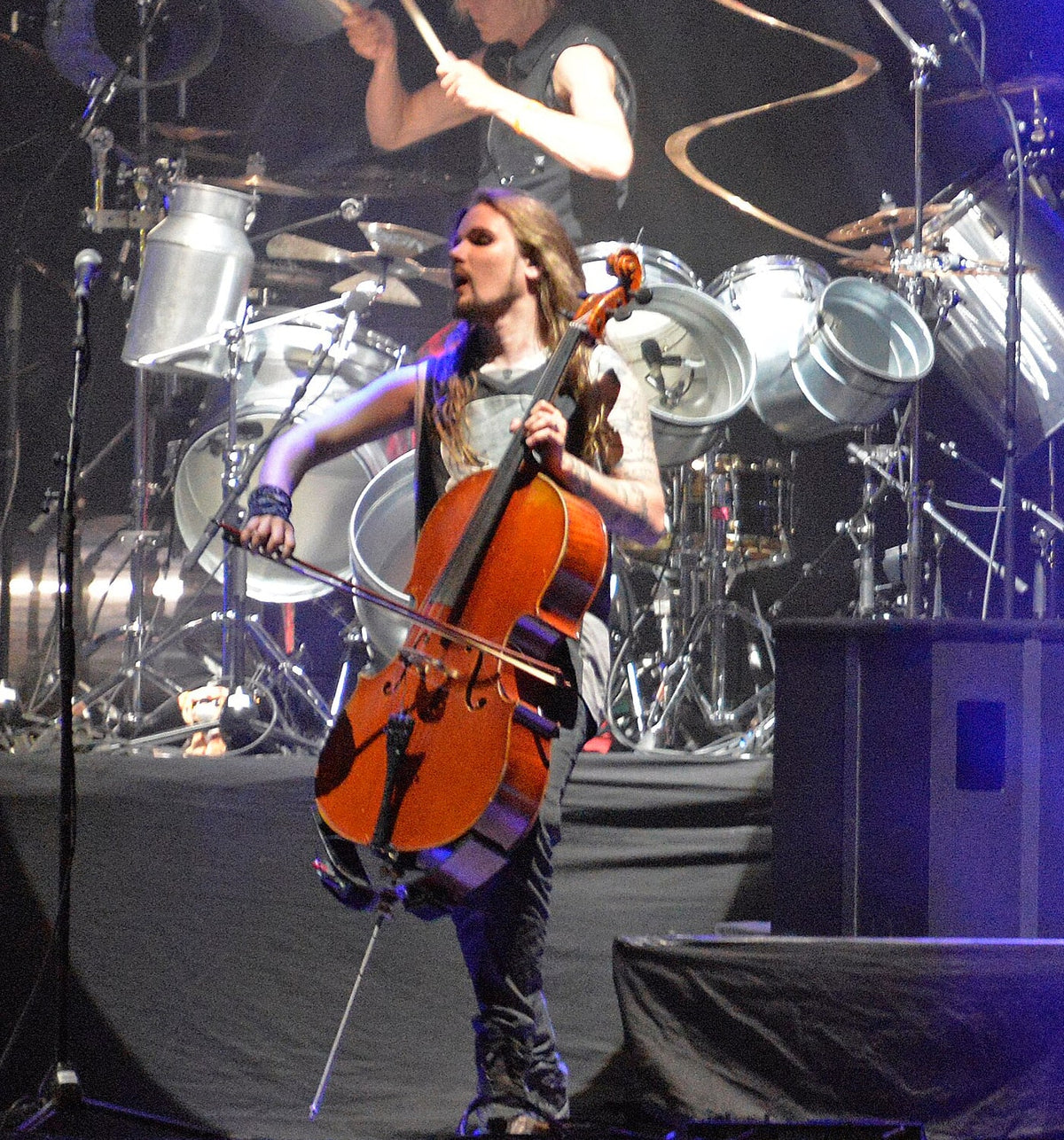 Perttu Kivilaakso van Apocalyptica speelt cello op Hellfest in Clisson in 2017, met lang bruin haar, een sik en een zwart mouwloos shirt voor een drumstel onder blauw podiumlicht.