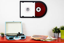 Zwarte lijst met lp "Golden Earring" hangt aan de muur, naast een blauwe platenspeler en stapels lp's.