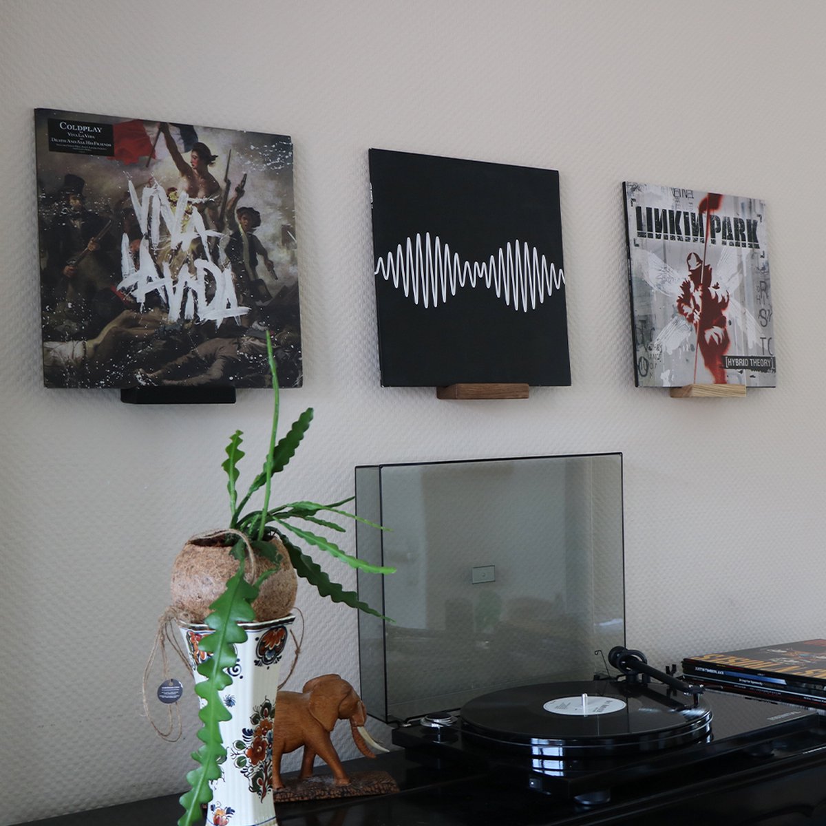 Drie platenhoezen hangen aan de muur, waaronder 'Viva la Vida' van Coldplay en 'AM' van Arctic Monkeys.