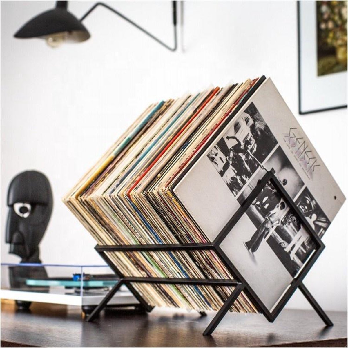 Zwart metalen platendrager met vinylplaten op een tafel, naast een zwarte sculptuur.