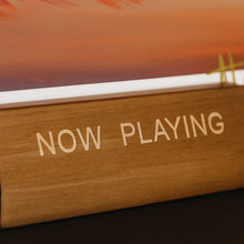 Close-up van de tekst "Now Playing" op een houten LP-standaard.